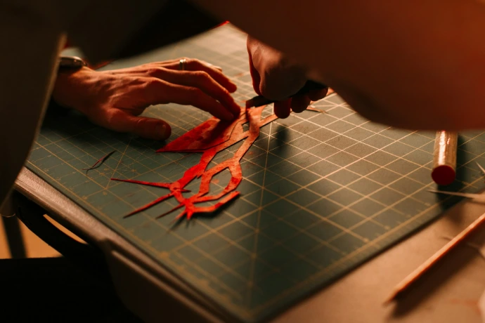 Hands carefully cutting intricate red paper design